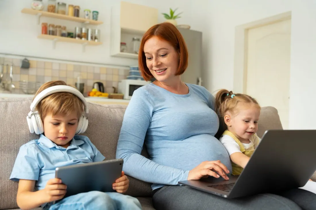 A parent working on a laptop at home alongside two young children