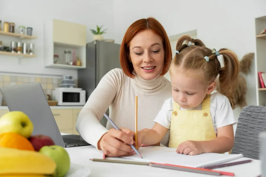 A parent and child drawing together at the kitchen table