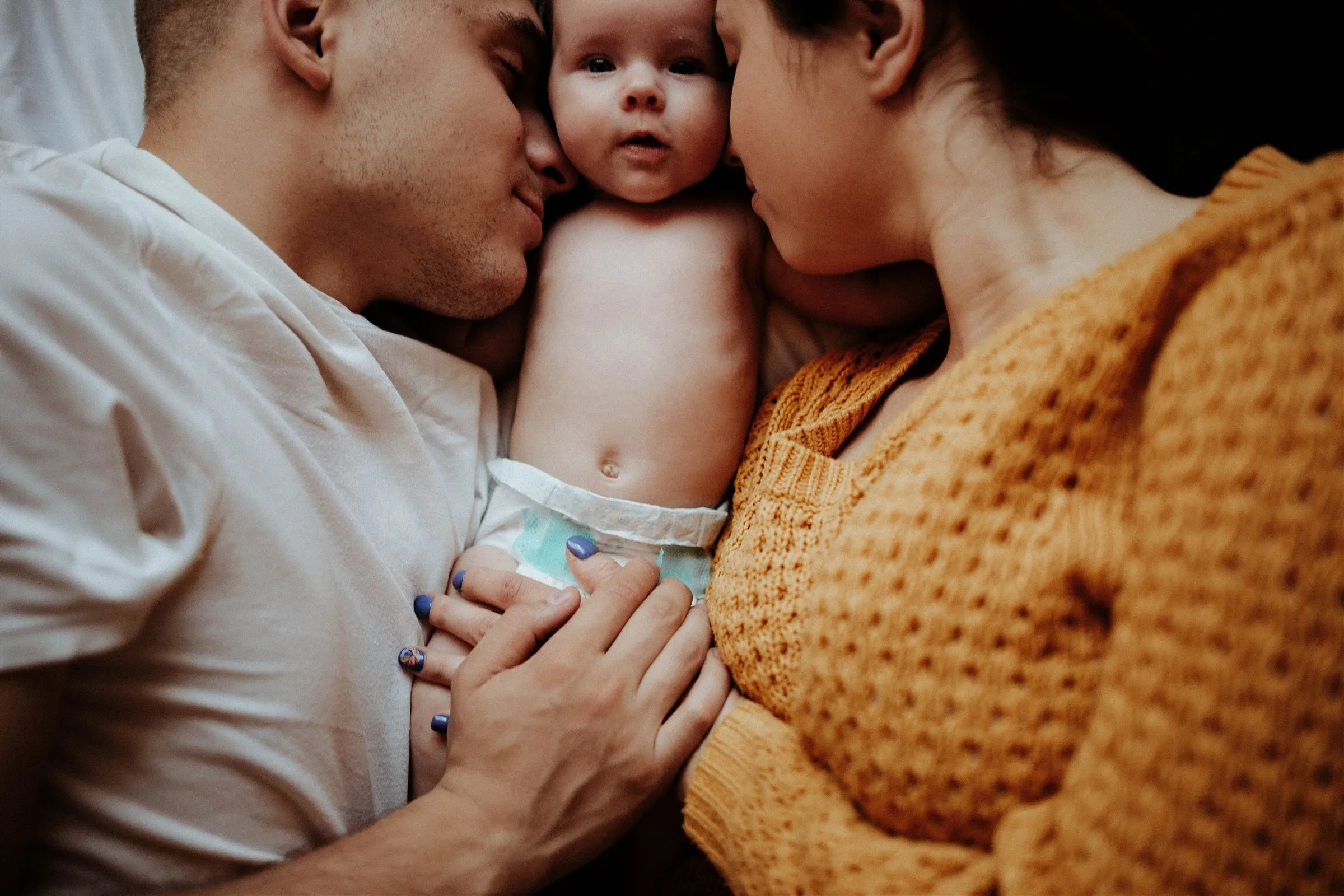 Zwei Eltern kuscheln eng mit ihrem Neugeborenen