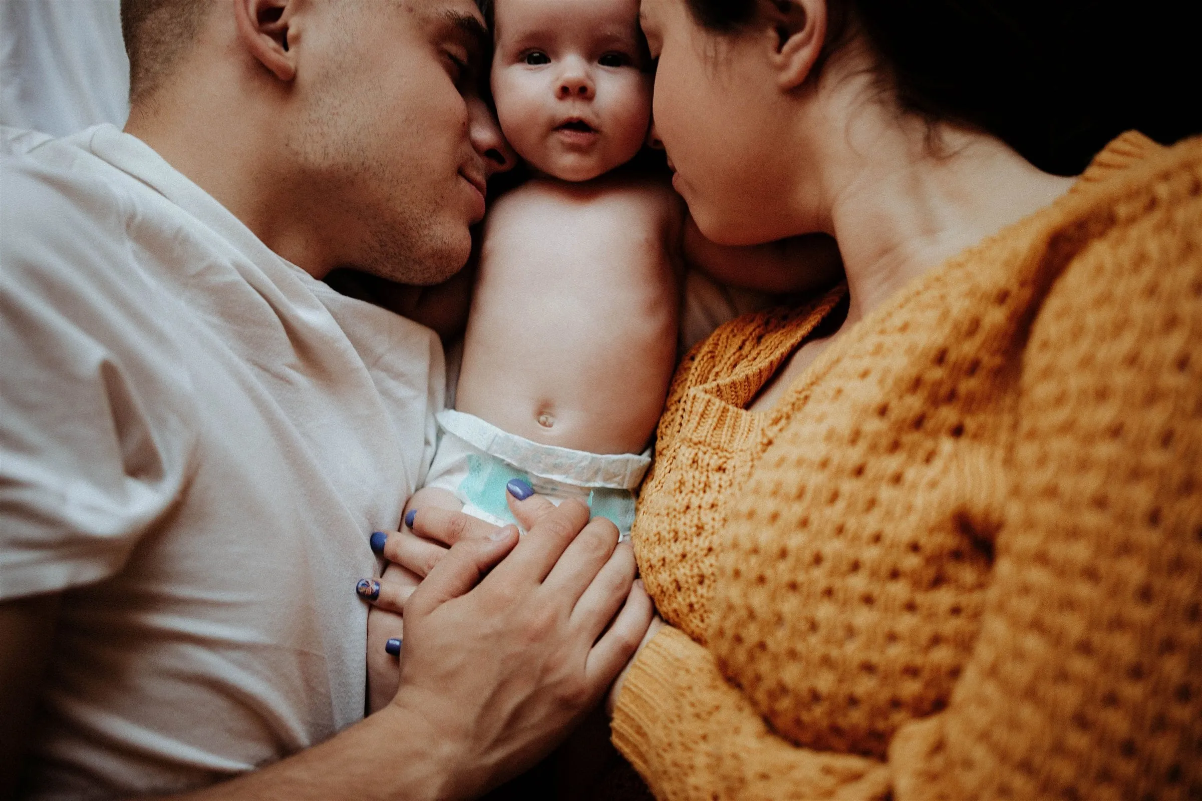 Two parents cuddled close around their newborn baby