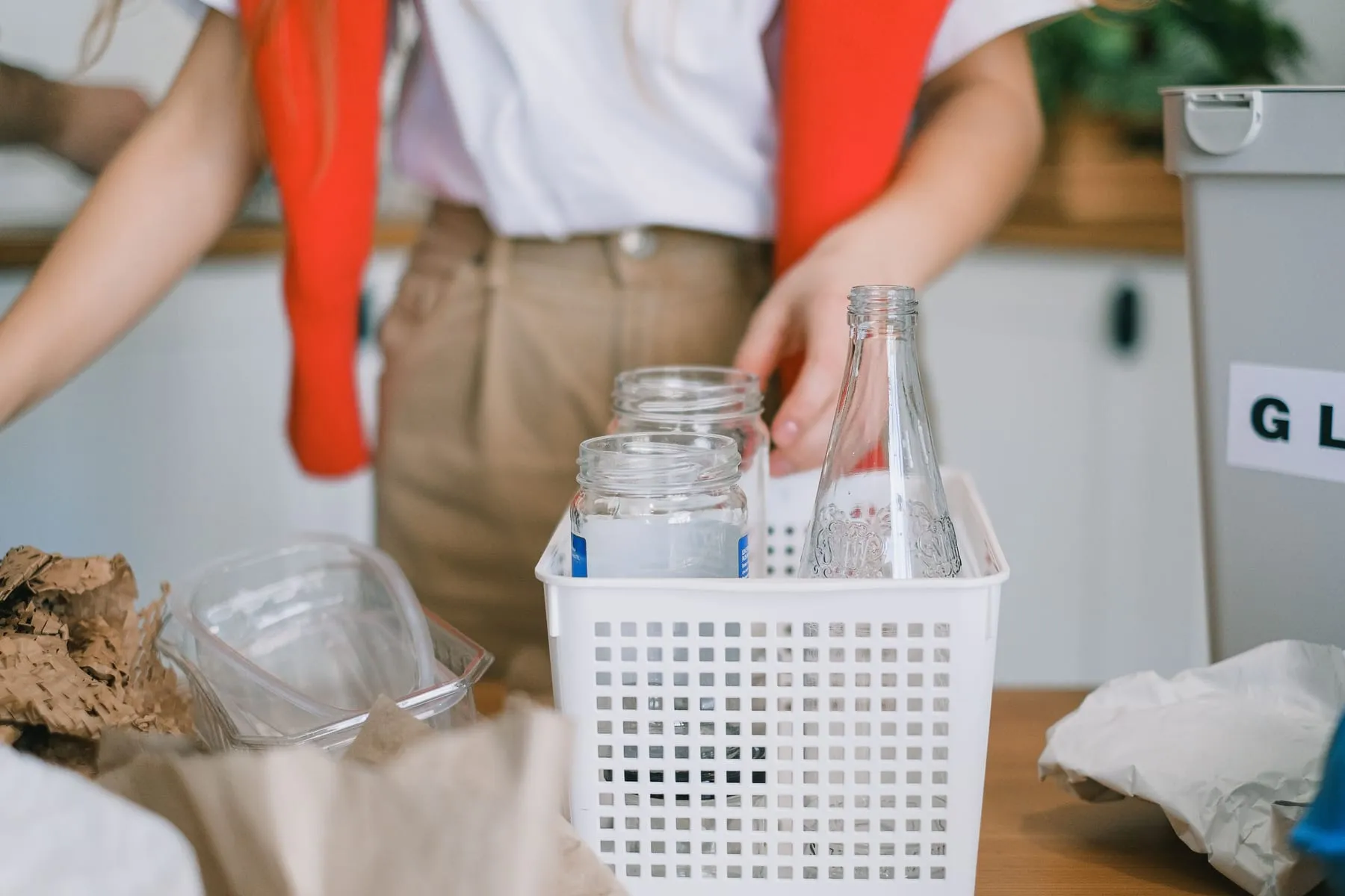 Glass jars and bottles being sorted into a basket for recycling in a bright kitchen